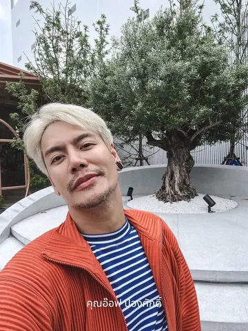 Aof Pongsak Rattanapong takes a close-up selfie with an olive tree visible behind him.