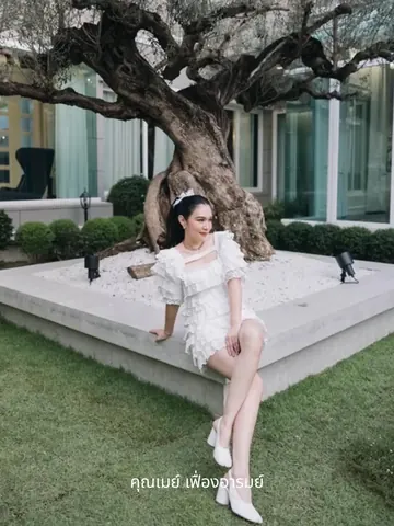 May fuangarom sits on the edge of a planter beneath a large olive tree.
