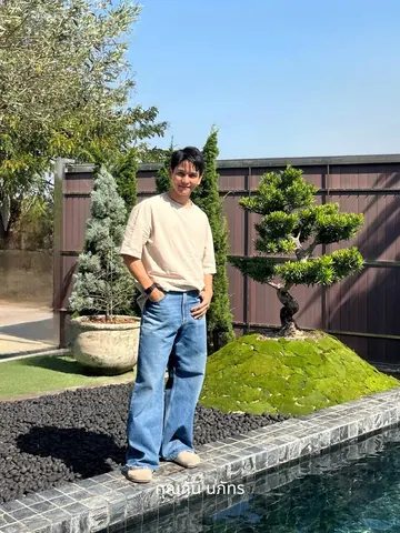 Gun Napat Injaiuea stands beside a sculpted shrub with a large tree visible behind him.